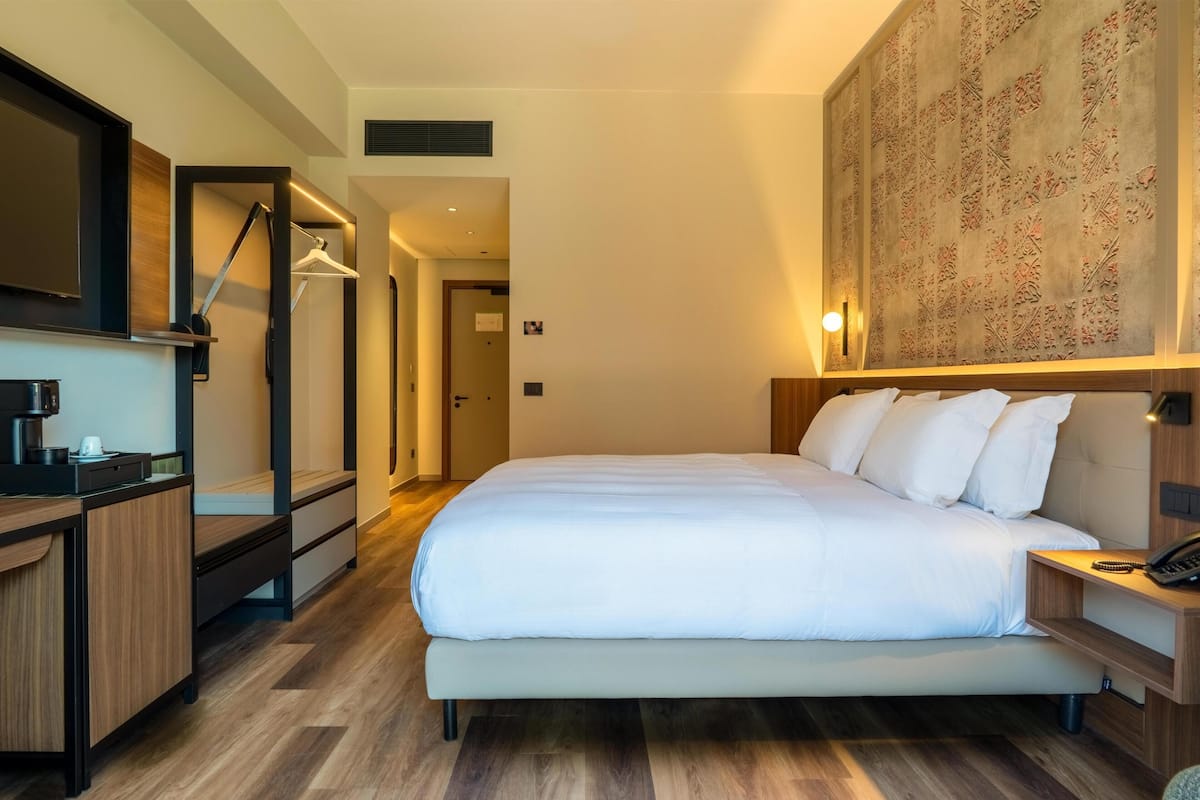 A hotel room with a bed, bedside table, desk, and a large wall-mounted artwork.