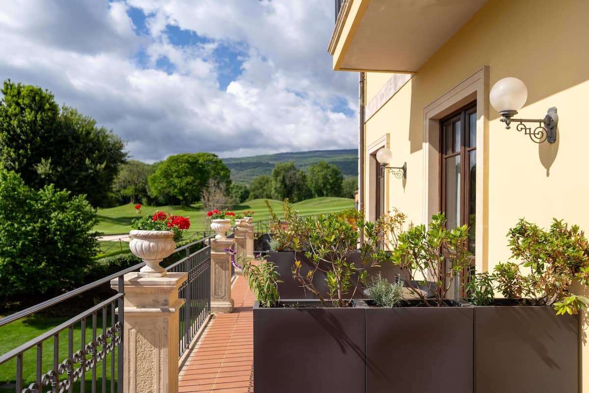 A balcony with a view of a green landscape, a railing, and a wall-mounted light fixture.