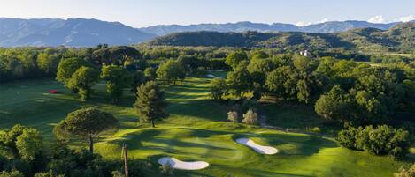 Un parcours de golf avec des bunkers de sable, des arbres et des montagnes qui se dessinent à l’horizon.
