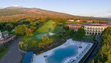Un campo da golf con piscina, circondato da edifici con tetti rossi e una montagna sullo sfondo.