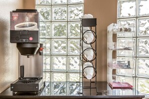 A coffee machine, a rack with cups, and a glass display case with items. - Rodeway Inn Ventura Midtown (Ventura)