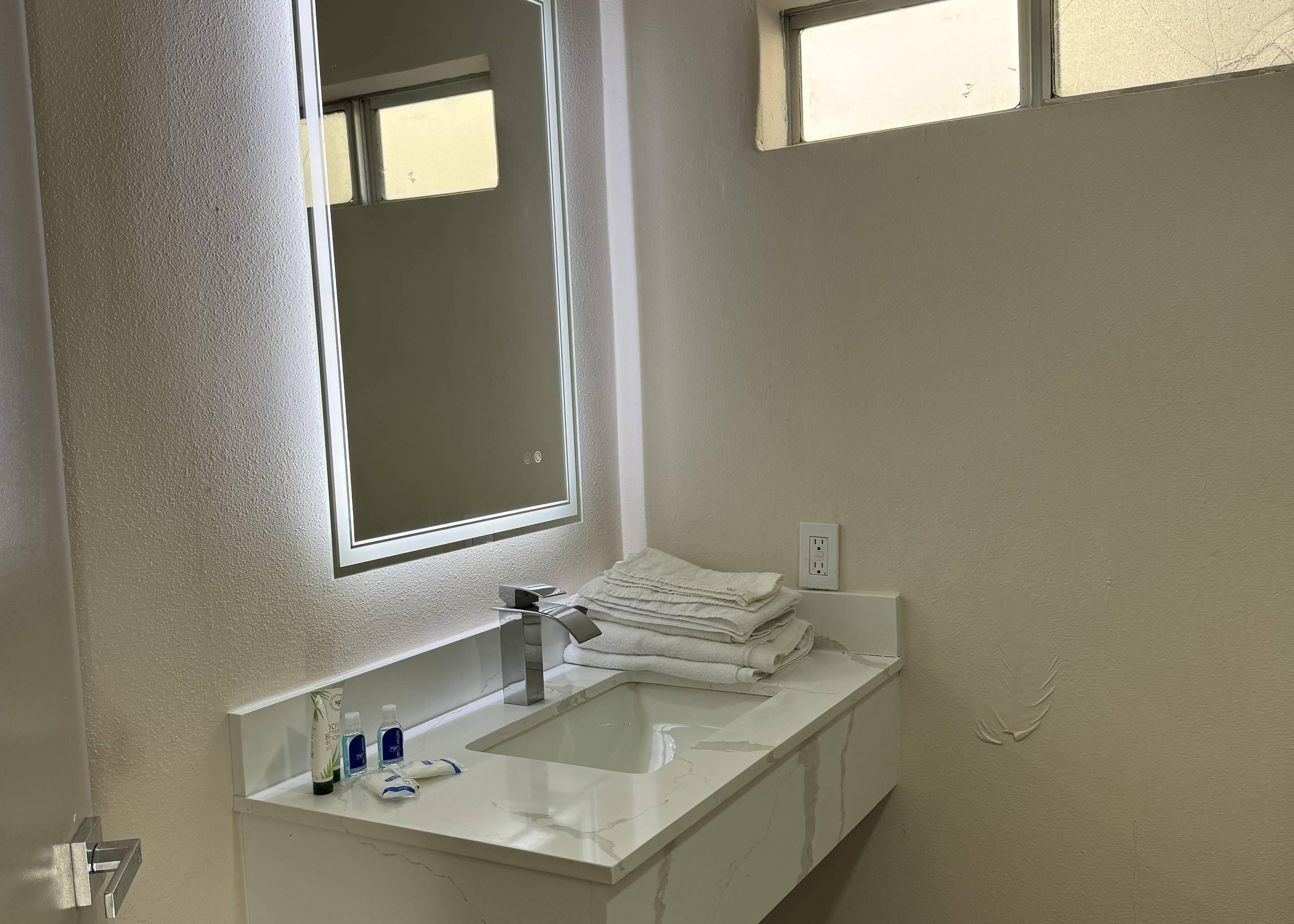 Un baño con lavamanos blanco, espejo y perchero.