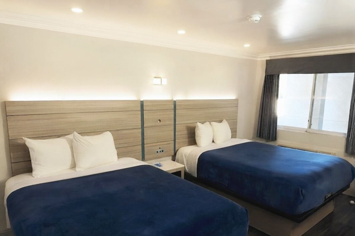 A hotel room with two beds, a wooden headboard, bedside lamps, and a window with curtains.