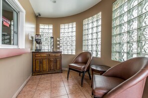 A room with a curved ceiling, a wooden cabinet, a coffee machine, two leather chairs, and large windows with a grid pattern.