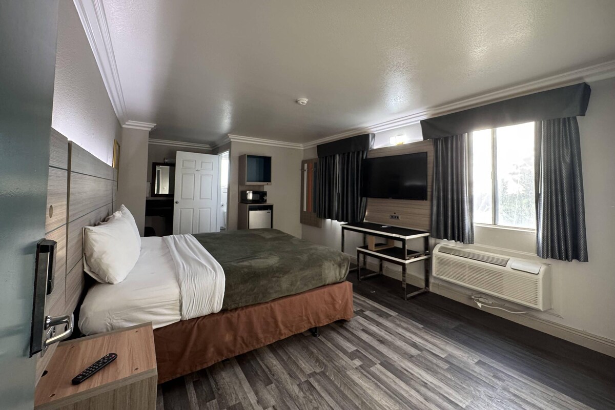A hotel room with a bed, a desk, a television, a window with curtains, and a door.