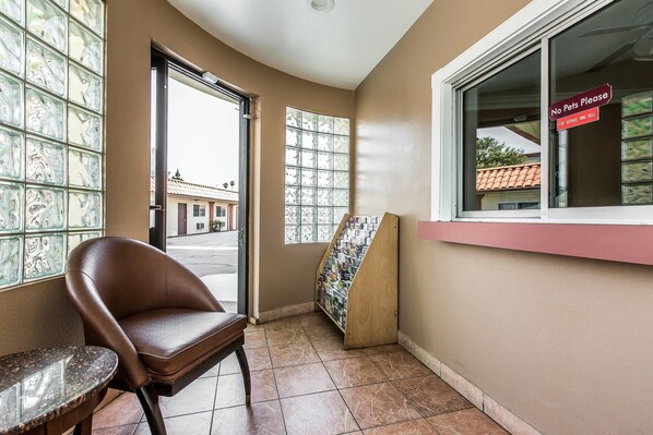 A corner of a room with a brown leather chair, a small table, a window with a 'No Pets Please' sign, and a bulletin board with pamphlets. - Rodeway Inn Ventura Midtown (Ventura)