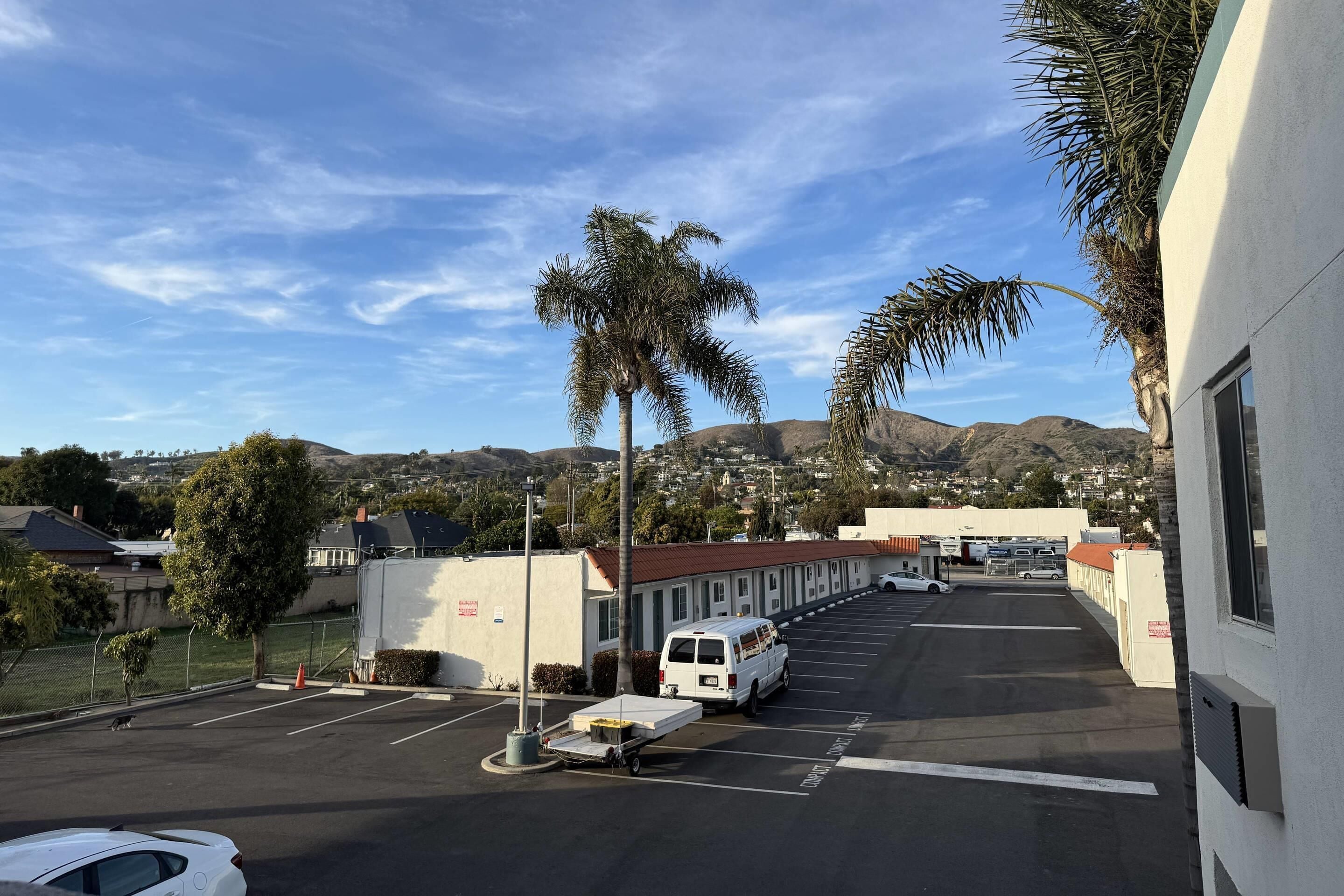 A parking lot with a white van, a white car, and a building with a red roof.