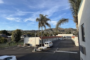A parking lot with a white van, a white car, and a building with a red roof. - Rodeway Inn Ventura Midtown (Ventura)