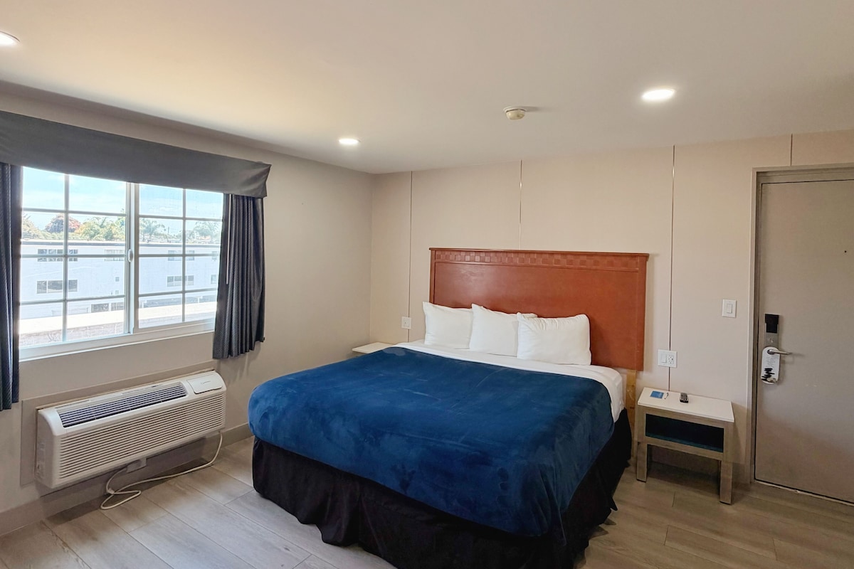 A hotel room with a bed, bedside table, and a window with curtains.