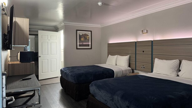 A hotel room with two beds, a desk with a computer, a TV, and a door leading to another room. - Rodeway Inn Ventura Midtown (Ventura)