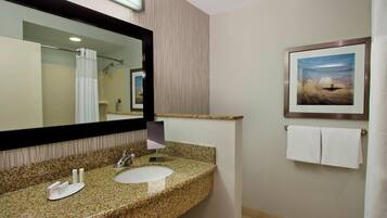 Une salle de bain avec un lavabo doté d’un plan de travail en granit, un grand miroir, un tableau encadré au mur et un porte-serviettes avec deux serviettes.