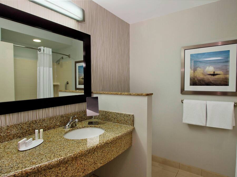 Une salle de bain avec un lavabo doté d’un plan de travail en granit, un grand miroir, un tableau encadré au mur et un porte-serviettes avec deux serviettes.