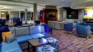 A hotel lobby with a seating area featuring sofas and armchairs, a television, and a bar area.