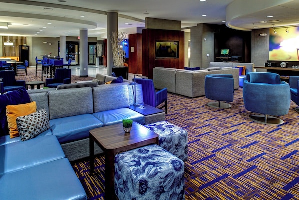 Un vestíbulo de hotel con una zona de estar que incluye sofás y sillones, un televisor y una barra.