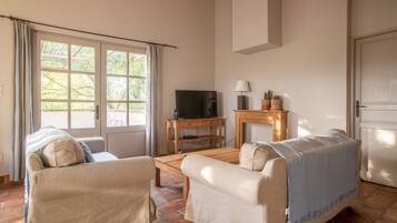A living room with two sofas, a TV on a wooden stand, a lamp, and a small table with plants.