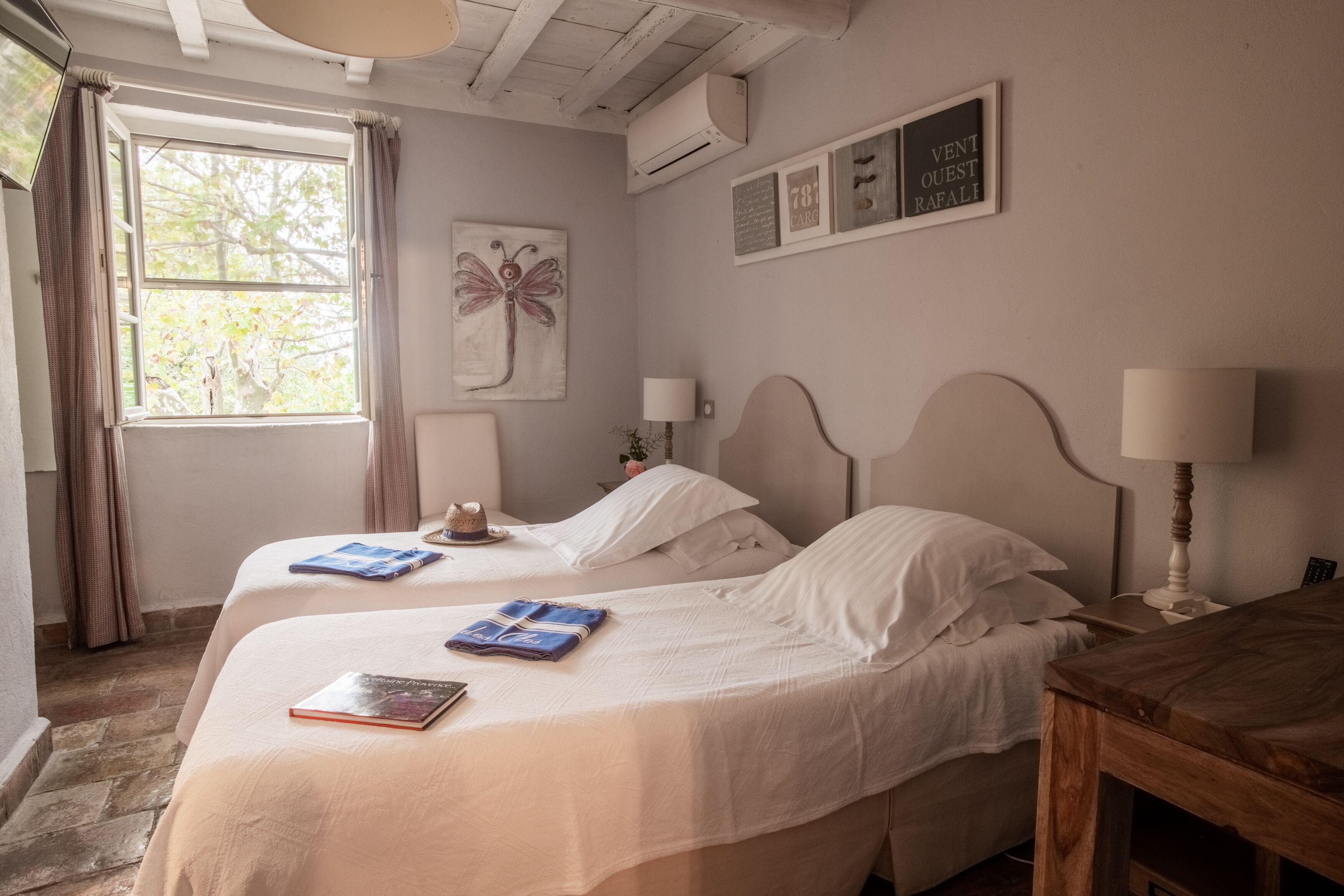 A bedroom with two beds, a wooden table, and a window with curtains.