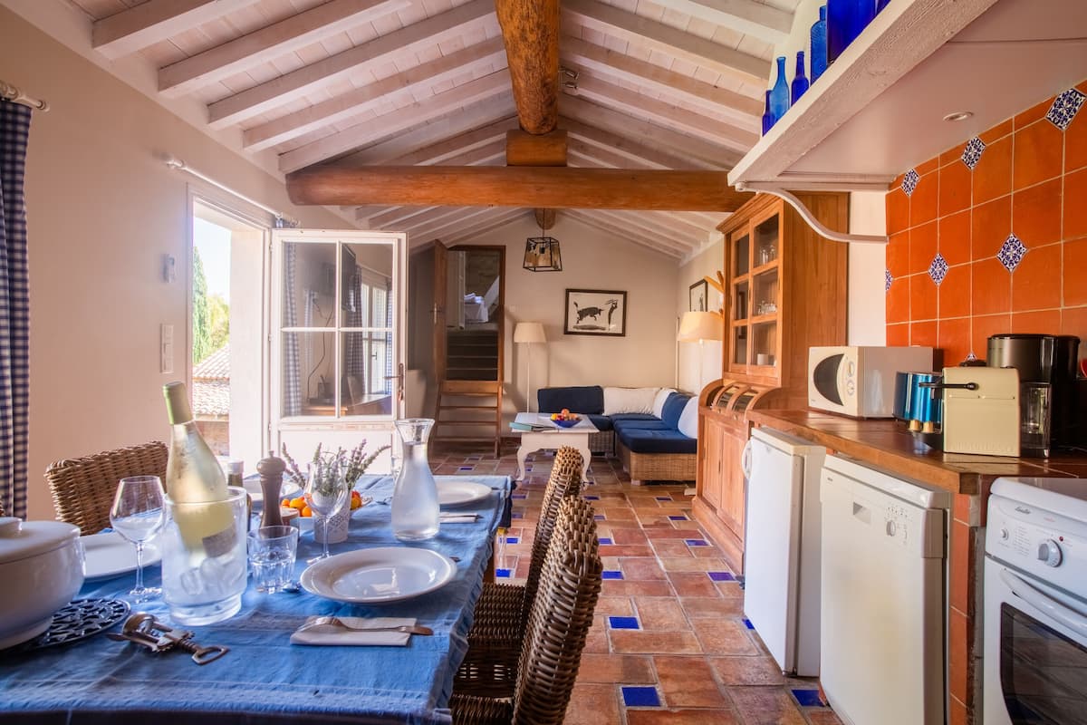 Un comedor con una mesa lista para dos, una cocina con electrodomésticos y una escalera que sube a un nivel superior.