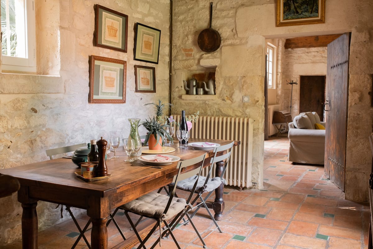 Un comedor rústico con una mesa de madera, sillas y piso de baldosas.