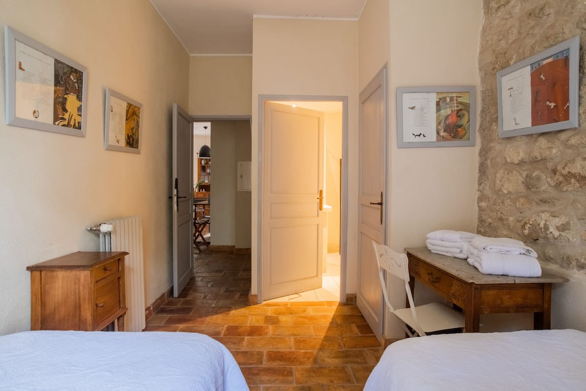 Habitación de hotel con dos camas, un aparador de madera, un radiador y una pared de piedra.