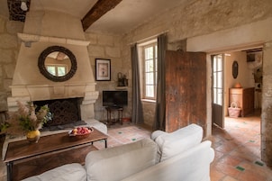Una sala rústica con chimenea de piedra, sofá de cuero blanco y televisor.
