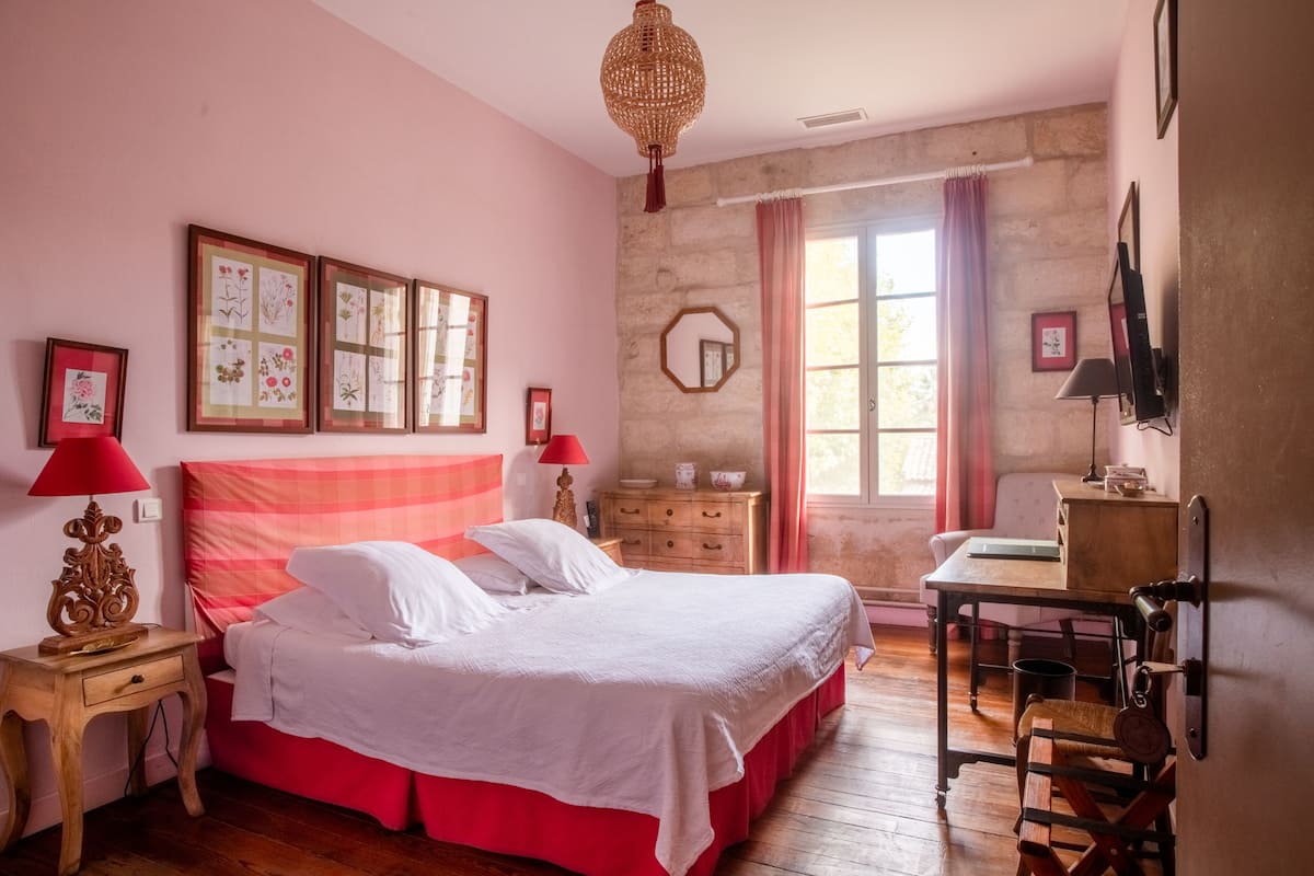 Un dormitorio con una cama, mesitas de noche de madera, un tocador, un escritorio, un espejo e impresiones enmarcadas de motivos botánicos en la pared.