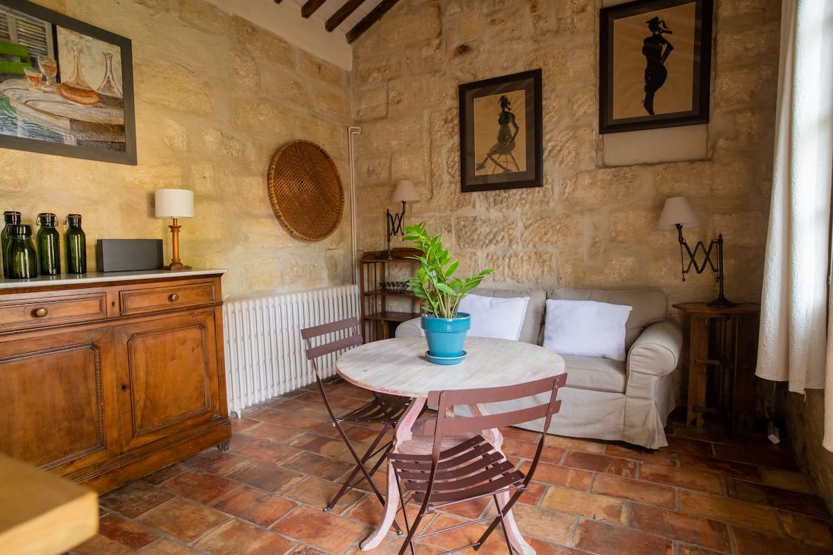 Una habitación rústica con pared de piedra, una mesa redonda de madera con sillas, un sofá blanco y un radiador.