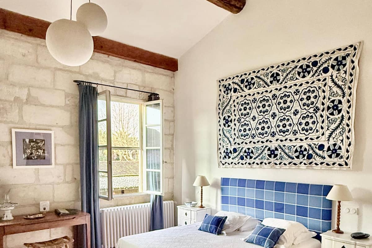 Un dormitorio con cama, mesitas de noche, escritorio, silla, radiador y ventana.
