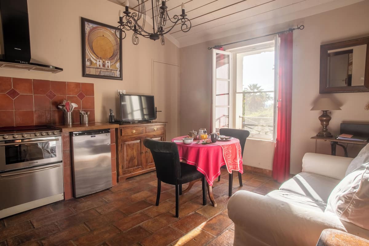 Cocina compacta con estufa a gas, horno y lavavajillas. Un comedor con sillas se encuentra cerca de una ventana con cortinas rojas.