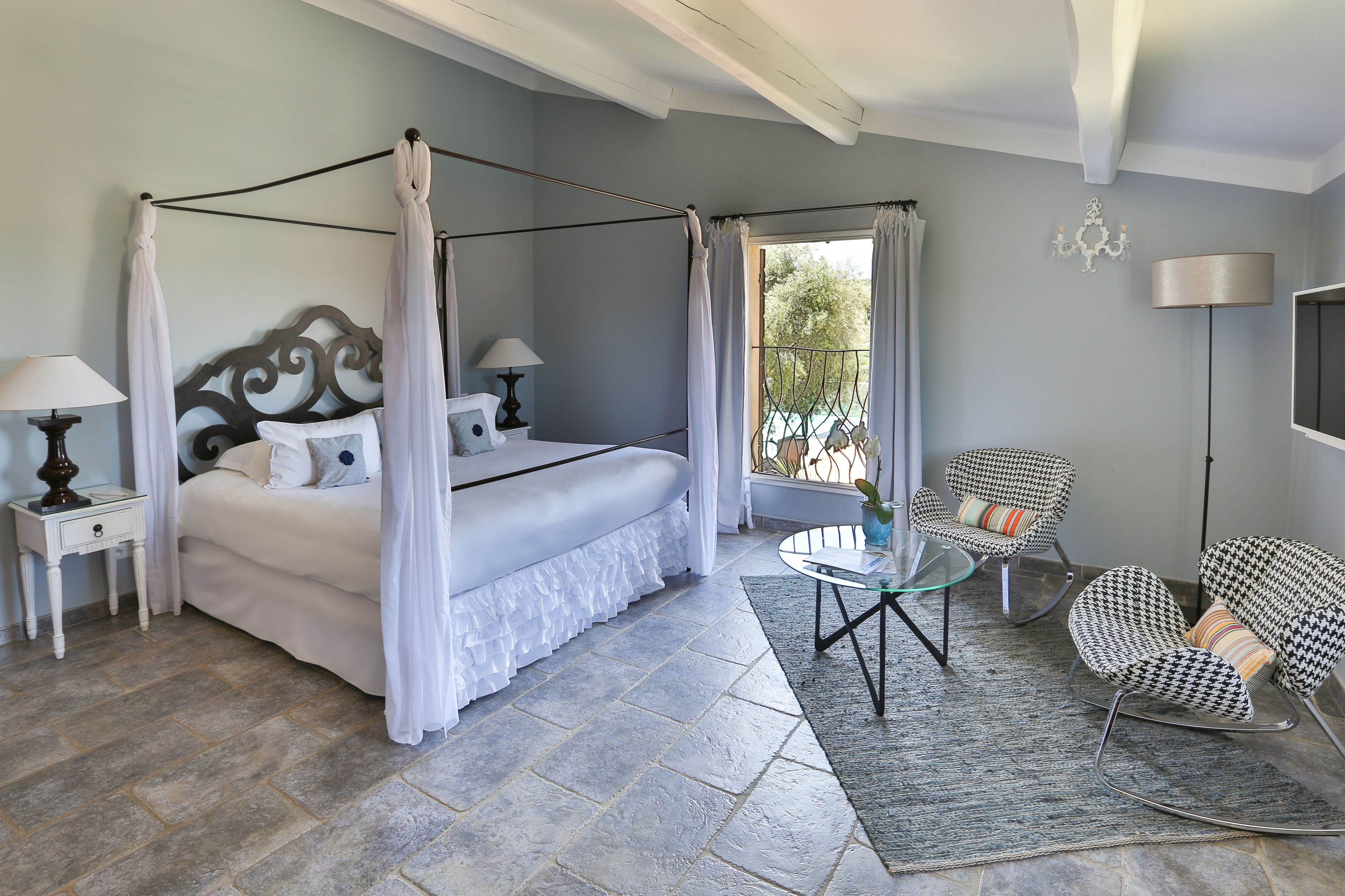 A bedroom with a four-poster bed, a glass coffee table, and two rocking chairs.