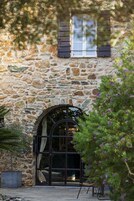 Un edificio de piedra con un gran arco de entrada, una ventana pequeña con contraventanas y una silla afuera.