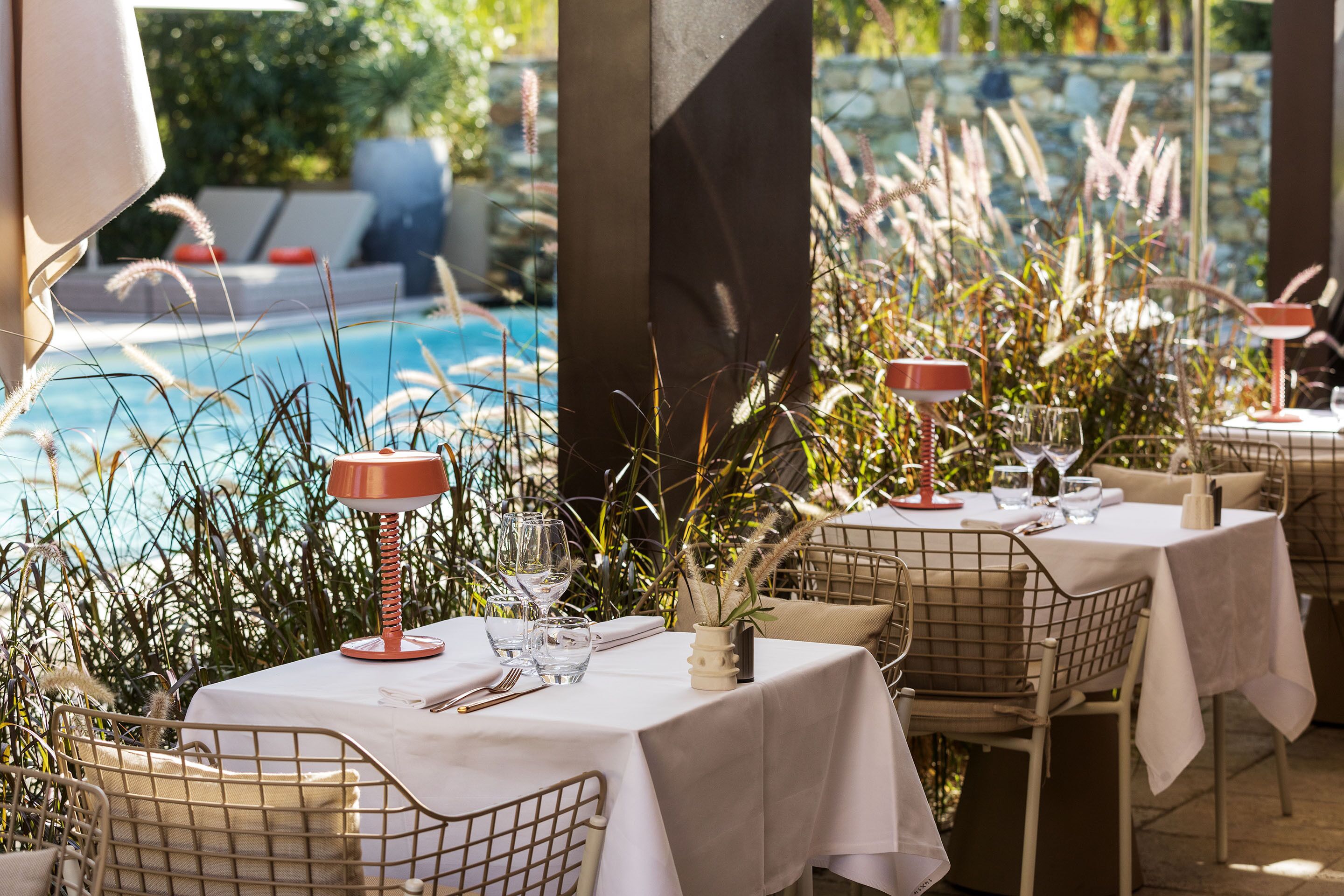 Outdoor dining tables with white tablecloths, metal chairs, and red lamps.