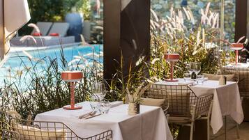Outdoor dining tables with white tablecloths, metal chairs, and red lamps.