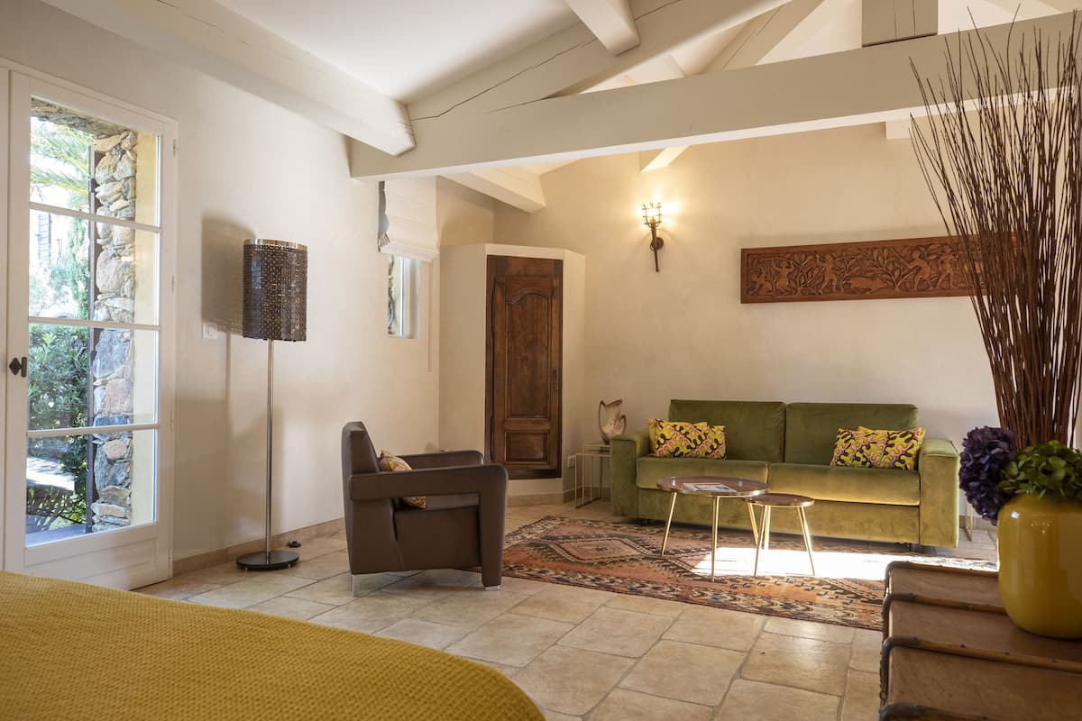 A living room with a sofa, armchair, and a coffee table. There is a door, a window, and a wall-mounted light fixture.