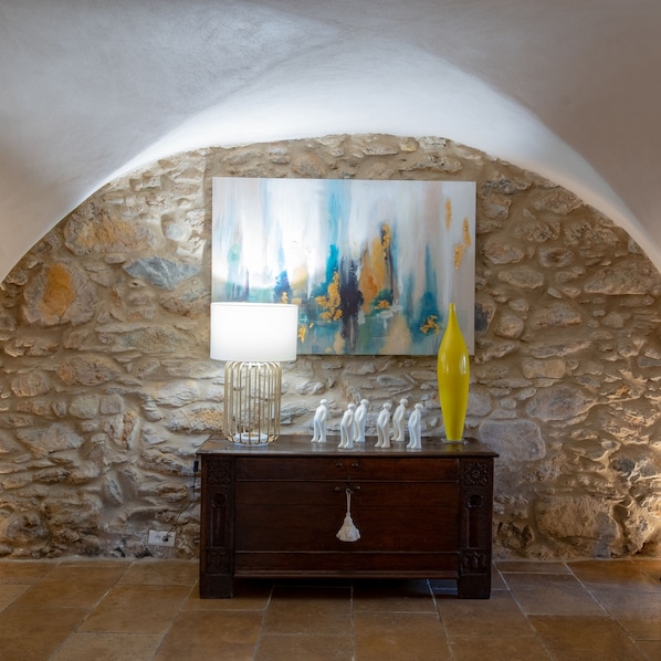 A stone wall with a painting, a lamp, and decorative figures on a wooden dresser. - La Dimora (Oletta)