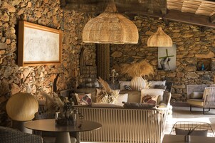 Un interior acogedor con pared de piedra, una zona de estar con cojines y una lámpara trenzada de gran tamaño.