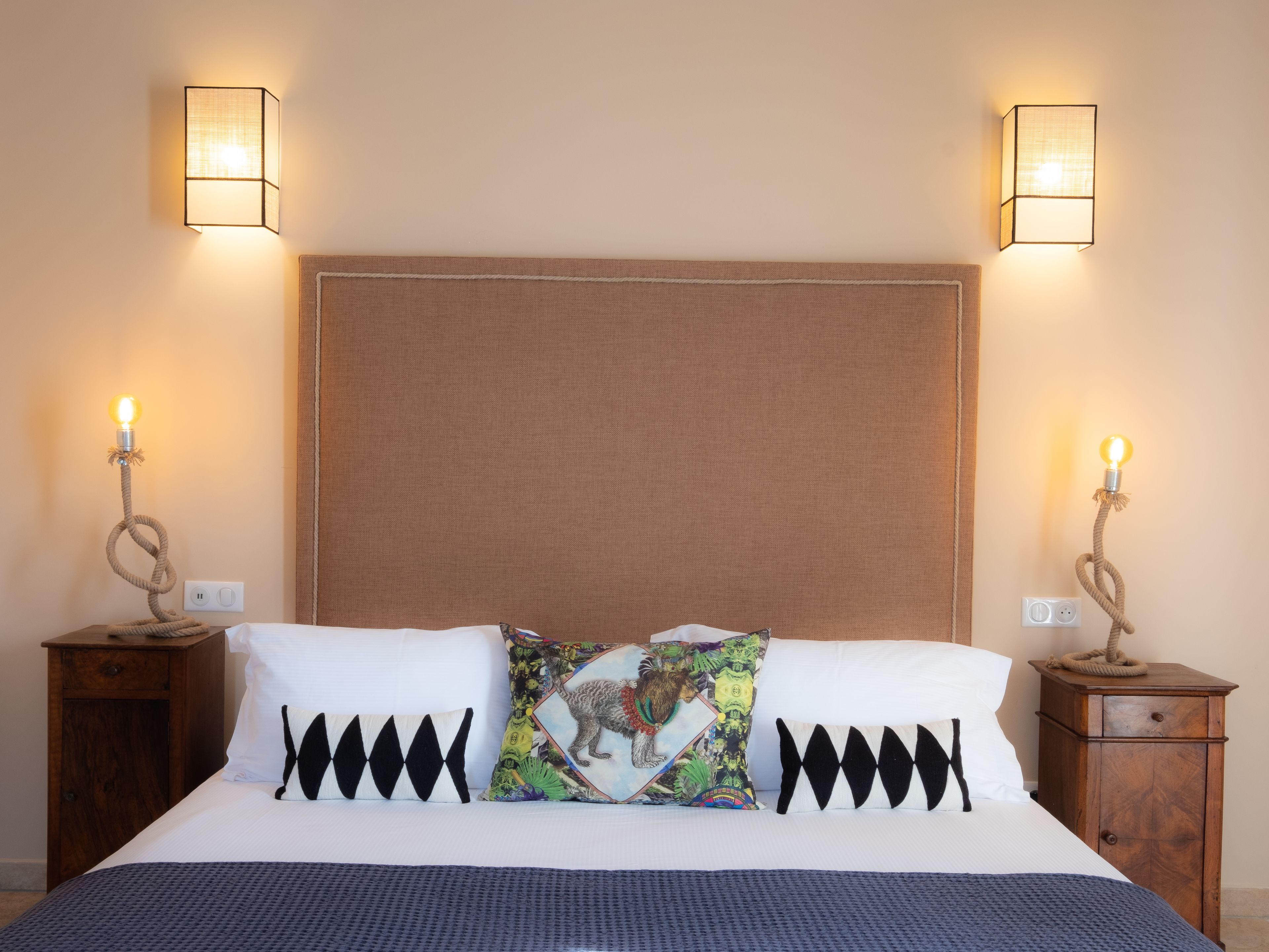 A neatly made bed with white and black pillows, two bedside tables with lamps, and a plain wall.