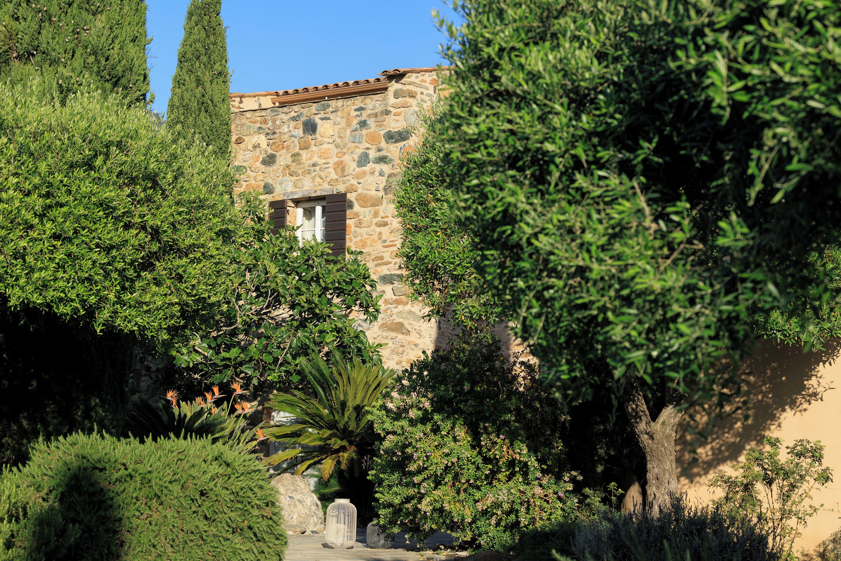Un bâtiment en pierre doté d’une fenêtre, entouré d’une végétation luxuriante et d’arbres.