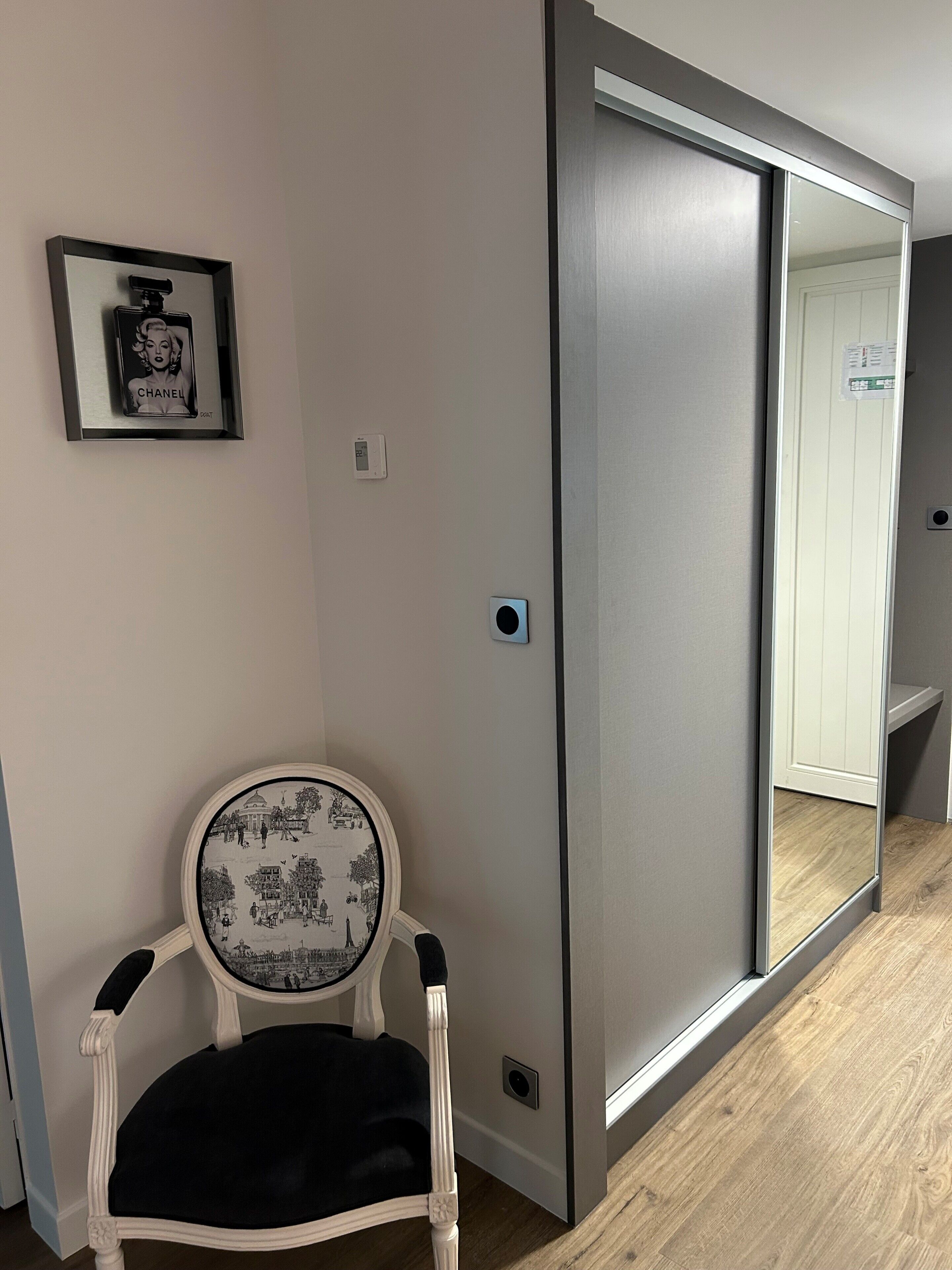 Una habitación con puerta corredera, un cuadro en la pared, un termostato y una silla con cojín estampado.