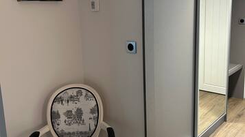 Una habitación con puerta corredera, un cuadro en la pared, un termostato y una silla con cojín estampado.