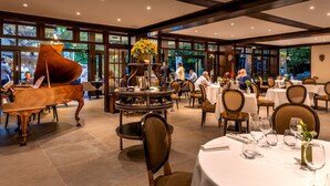 A restaurant with a grand piano, round tables, and a view of the outdoors. - Hostellerie Du Royal Lieu (Compiègne)