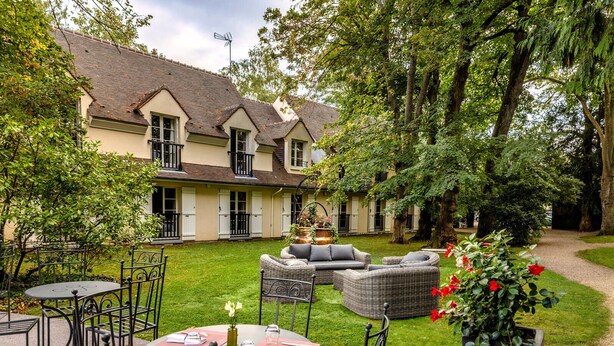 A courtyard with outdoor seating, a building with a tiled roof, and lush greenery. - Hostellerie Du Royal Lieu (Compiègne)