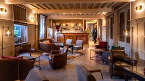 A spacious lounge area with leather sofas, a bar with a variety of bottles, and a view of the outdoors through large windows. - Hostellerie Du Royal Lieu (Compiègne)