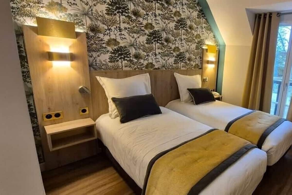 A hotel room with two beds, a wooden nightstand, a chair, and a window with curtains.