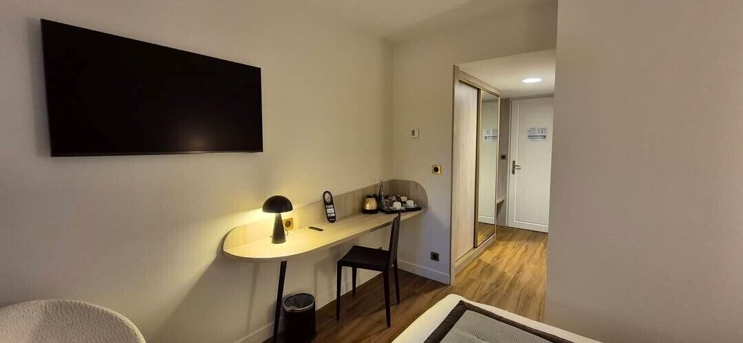 Una habitación con escritorio, silla, lámpara y televisor fijado en la pared.