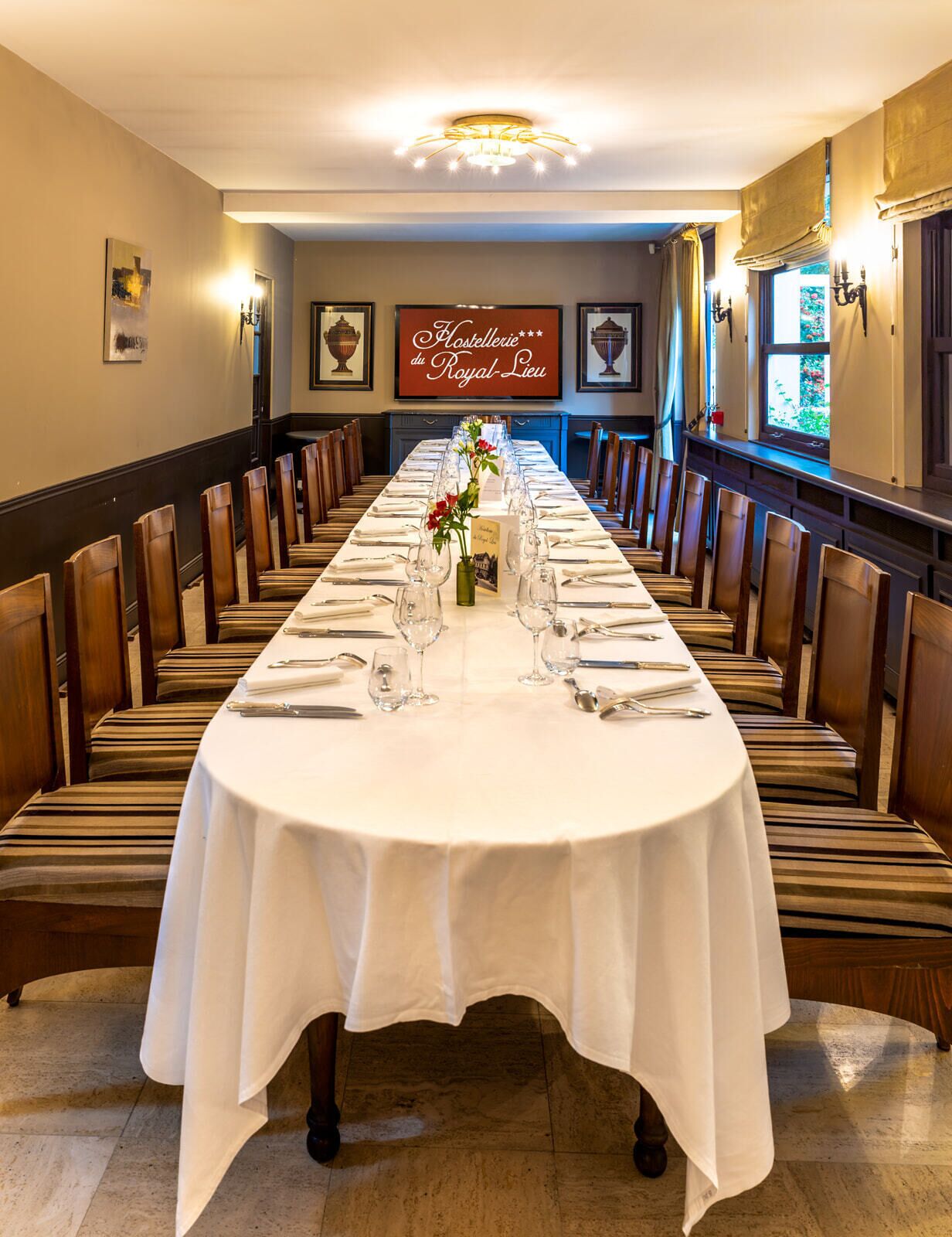 A long dining table set for a meal in a room with wooden chairs, a chandelier, and framed artwork on the walls.