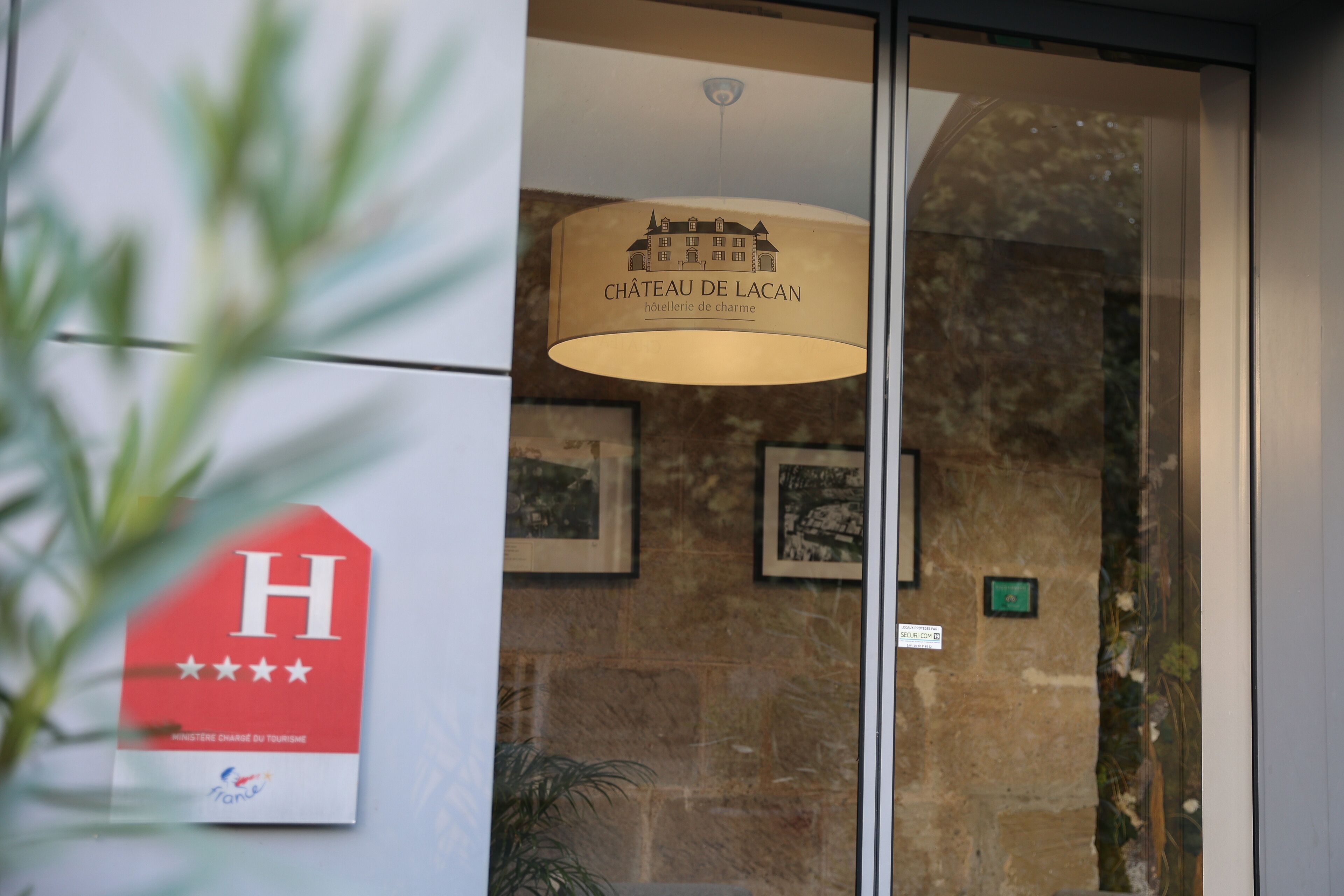 A hotel entrance with a sign reading "CHÂTEAU DE LACAN" and a red sign with a white 'H' and stars.