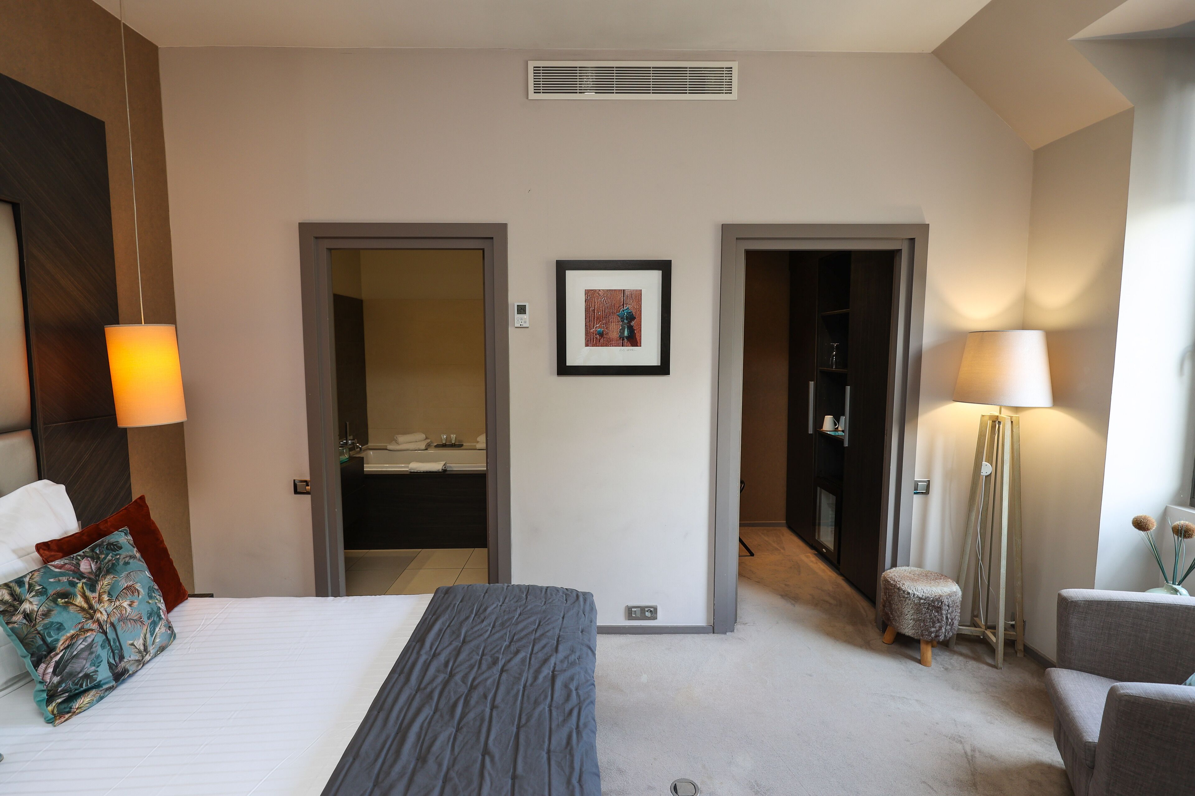 Een hotelkamer met een bed, een bureau, een stoel, een lamp en een schilderij aan de muur.