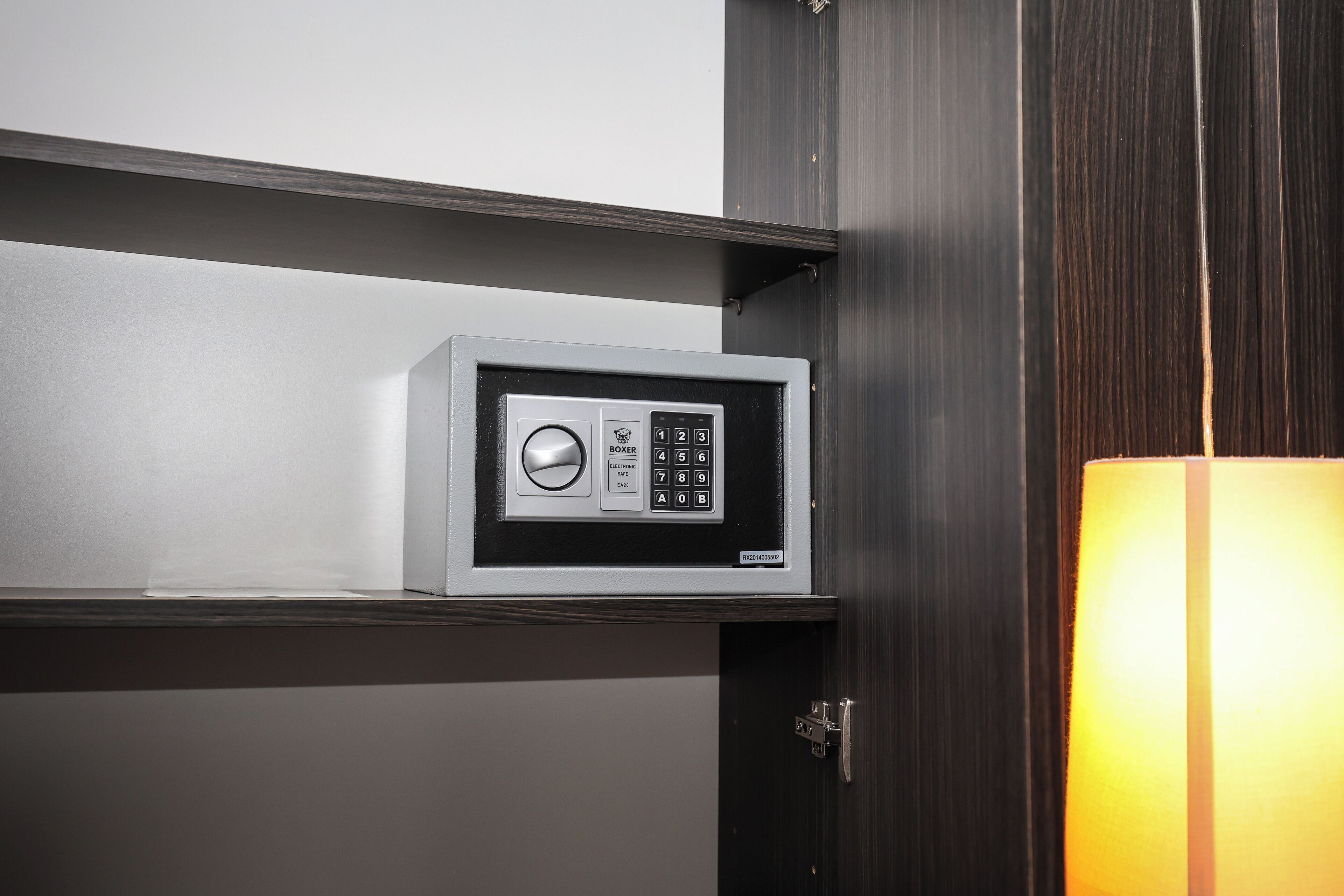 Eine Minibar mit digitaler Tastatur und kleinem Bildschirm, in einem Raum mit Holztür und einer hellen Lampe.