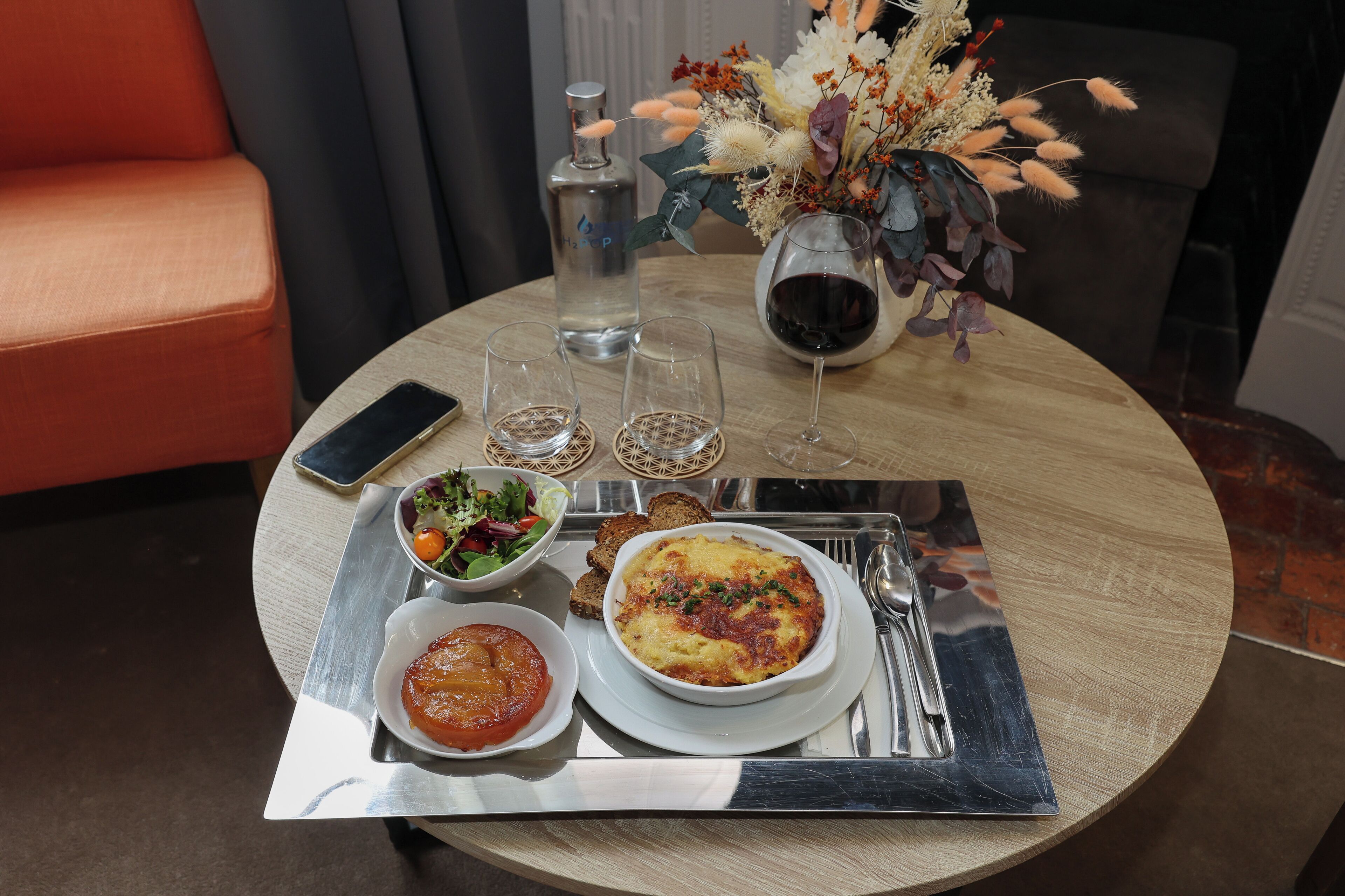 Een eettafel met diverse gerechten, waaronder een salade, brood en een kom soep. Ook staan er wijnkaraffen, een waterfles en een vaas met gedroogde bloemen op tafel.