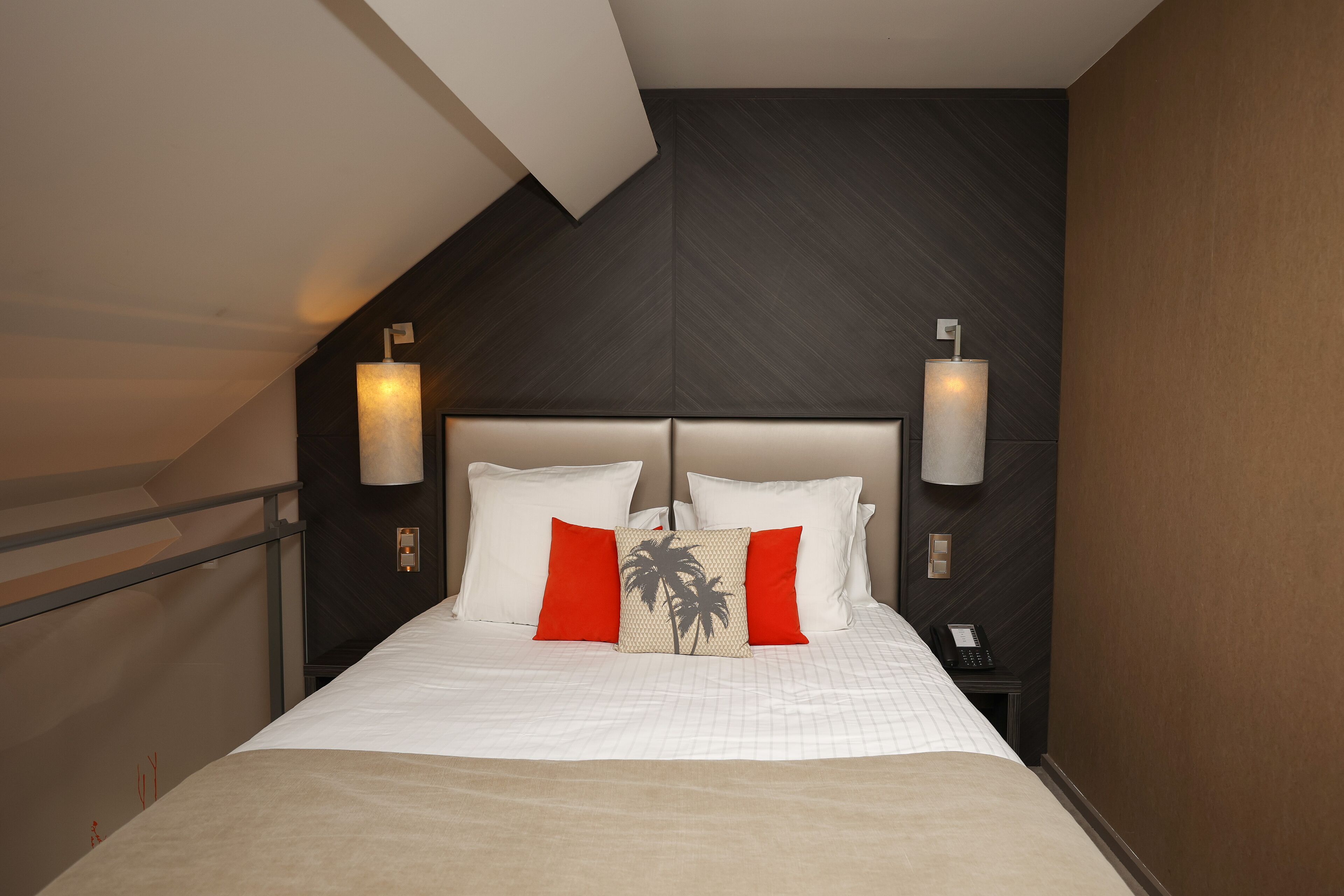 A hotel room with a bed, two bedside lamps, a nightstand with a phone, and a wall with a textured pattern.